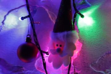 Una toma de cerca de una decoracion de navidad y fin de año con una cara de santa claus  rodeado de varias luces con bombillos de varios colores y bolas de navidad en la oscuridad
