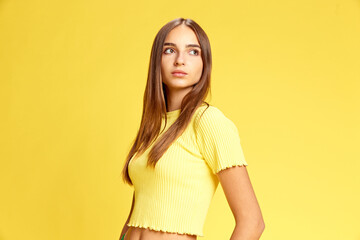 Obraz premium Looks to future and perspectives. Portrait of beautiful confident young lady looking away against sunny yellow background. Concept of human emotions, business, beauty and fashion, sales season. Ad