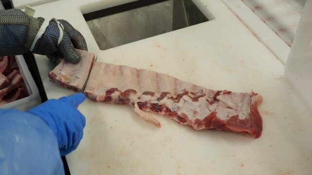 Butcher cuts pork ribs with knife at meat processing factory