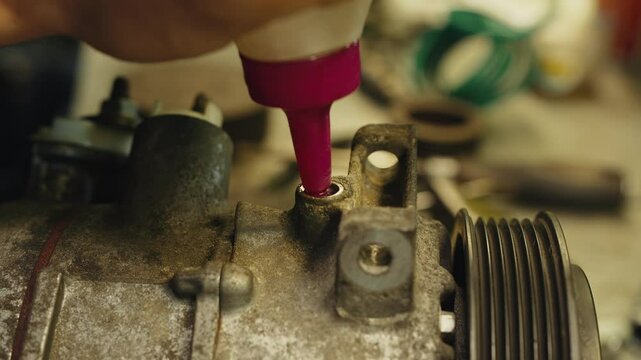 The technician fills the air conditioning compressor with oil using an oil can
