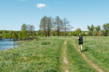 Fototapeta premium Young fitness woman running on a path near the river to keep fit. A runner trains in the midst of beautiful nature.