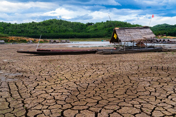 A dried-up lakebed with several wooden platforms and small huts built on it. Some boats are grounded on the cracked mud. In the background, there are hills covered in greenery.