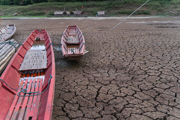 The ground is cracked and parched, with a network of deep fissures. Several traditional wooden boats are beached on the dried-up water body, highlighting the severity of the drought.