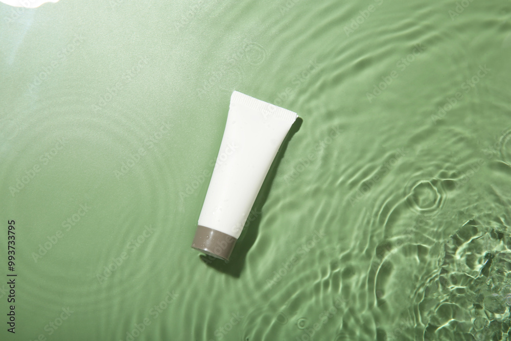 Poster Tube with cream in water on light green background, top view. Cosmetic product