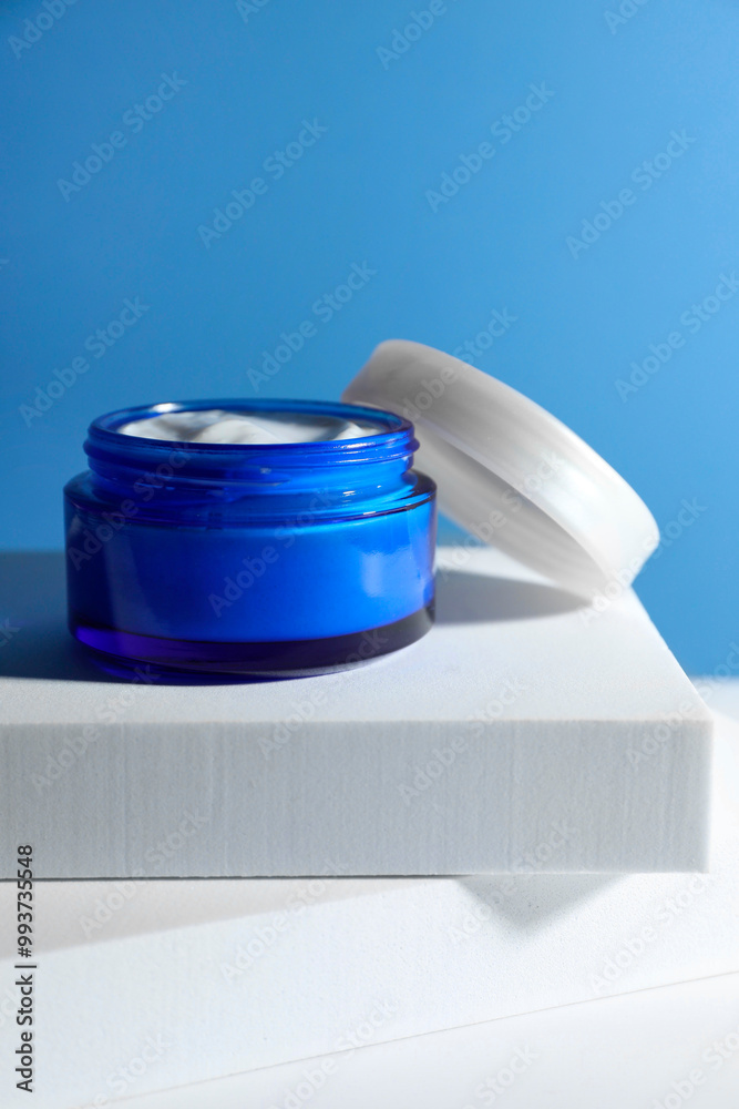 Poster Stylish presentation of face cream in jar against light blue background