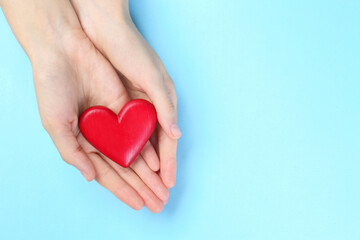 Woman holding red heart on light blue background, top view. Space for text