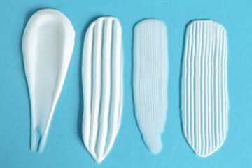 Smears of cosmetic products on light blue background, flat lay