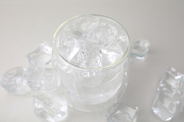 Refreshing water in glass with ice cubes on light background, closeup