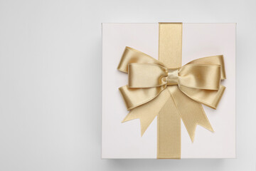 Gift box with golden bow on light grey background, top view. Space for text