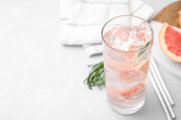 Refreshing water with grapefruit and rosemary in glass on light table, closeup. Space for text