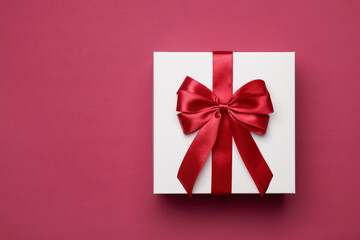 Gift box with red bow on burgundy background, top view. Space for text
