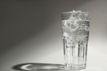 Refreshing water with ice in glass on grey background. Space for text