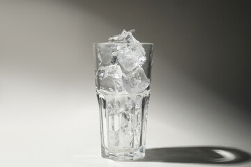 One glass with ice for refreshing drink on grey background