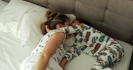 Funny little boy disturbs sleeping mother on double bed at home. Tranquil woman with adorable young son tries to sleep in bedroom. Morning relaxation