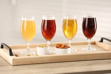 Glasses with different types of beer and snacks on wooden table indoors