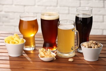Glasses with different types of beer and snacks on wooden table against white brick wall