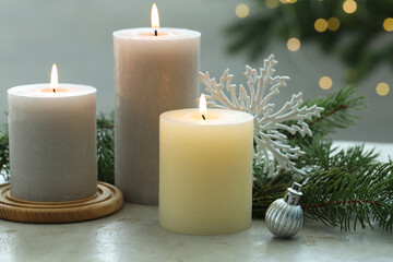 Burning candles, baubles and fir tree branches on white textured table, closeup