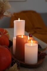 Tray with many burning candles and autumn decor on wooden table indoors, closeup