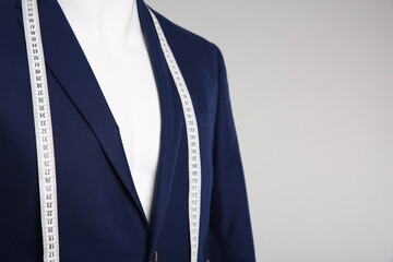 Male mannequin with elegant suit jacket and measuring tape on grey background, closeup. Space for text