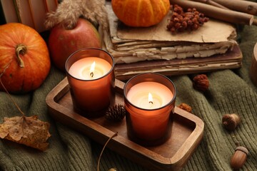 Burning candles, old books and autumn decor on green sweater