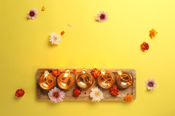Diwali celebration. Diya lamps and beautiful flowers on yellow background, flat lay