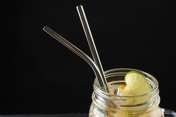 Tasty refreshing drink with straws in mason jar on black background, closeup