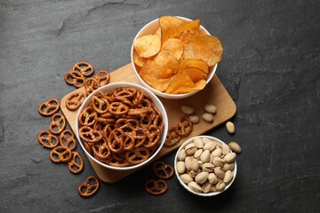 Delicious pretzel crackers and other snacks on black table, flat lay