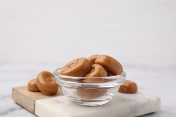 Tasty hard toffee candies in bowl on white table, closeup