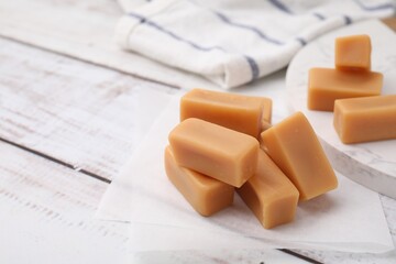 Tasty sweet caramel candies on white wooden table, closeup. Space for text