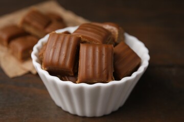 Tasty sweet caramel candies in bowl on wooden table, closeup