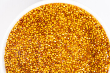 Traditional French Dijon mustard in a plate on a white background, top view.