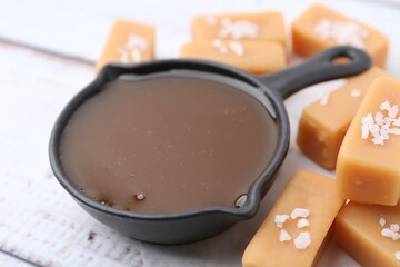 Tasty salted caramel in gravy boat and candies on table, closeup