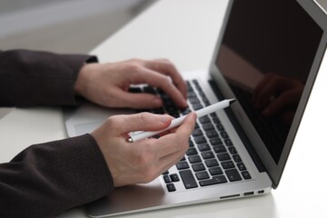 Businessman using laptop at white table indoors, closeup. Modern technology