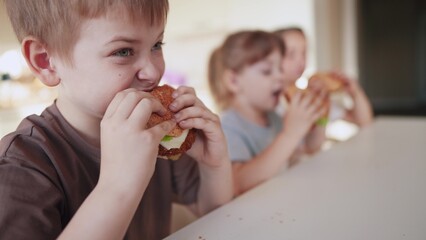 children eat burgers. fast food burger. a group of small children in the kitchen greedily eat fast food fun burgers. big family small kids having breakfast in the morning in the kitchen eating burger