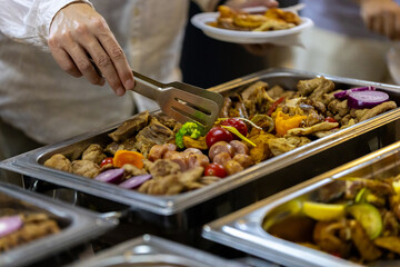 A person serving colorful grilled meats and vegetables at a festive outdoor gathering during a warm summer evening