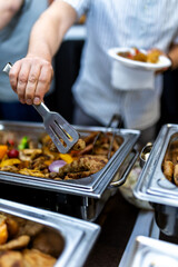 A person serving a variety of delicious dishes from a buffet setup during a lively gathering in an indoor setting