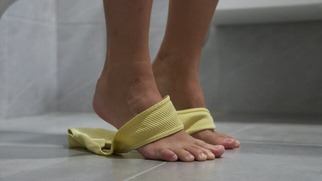 Close up low angle of legs of young white woman who is sitting on toilet in restroom. Shorts with panties are falling down. Concept of natural defecation