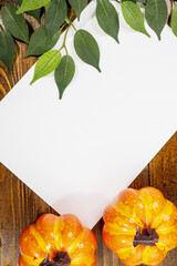 white sheet of paper on wooden background with halloween pumpkins and leaves