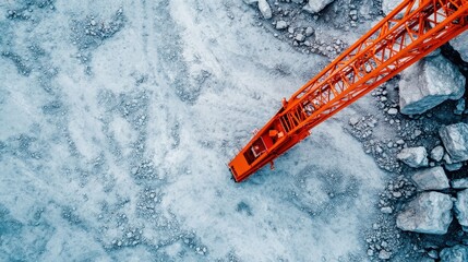 A striking aerial photograph capturing a bright orange crane operating on rough, rocky terrain, encapsulating the rugged environment and industrial machinery.