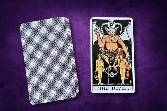 Carte de tarot "Le Diable" du jeu Rider-Waite, symbolisant la tentation et les d&eacute;sirs mat&eacute;riels. Carte sur fond violet textur&eacute; &agrave; c&ocirc;t&eacute; d'une autre carte face cach&eacute;e.