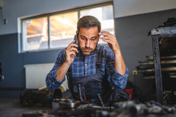 mechanic inspect car engine with tool at garage and talk on cellphone