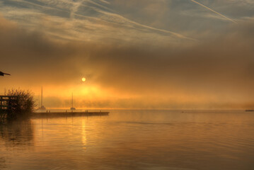 Morgendämmerung mit Nebel über einem See mit Booten und Steg