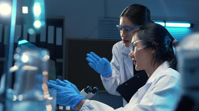 Two scientists in lab coats and safety glasses examining data on a computer screen in a laboratory setting
