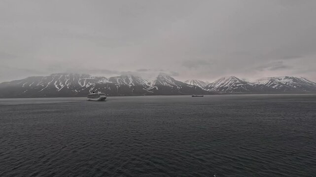 Isfjord, Svalbard, Spitzbergen, Norway - 2024: VIKING STAR cruise ship in port harbour at anchor departing on foggy overcast cloudy day in front of snow covered mountains