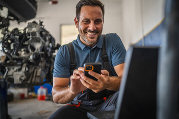 Car mechanic happily use mobile phone in garage near engine workspace