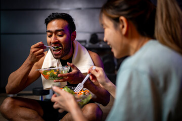 Two men and women are eating a vegetable salad together after exercising..