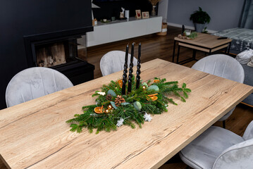 A Christmas decoration made of coniferous branches and a piece of wood, lying on the table in the dining room.