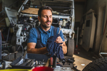 car mechanic holding cloth clean tools with open engine in background