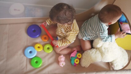 a group of children baby twins play pyramid toys in a crib arena sit. happy family kid dream concept. group of baby brother sister play pyramid sitting at home in the game room lifestyle