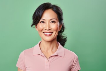 Fototapeta premium Portrait of a smiling asian woman in her 40s wearing a sporty polo shirt isolated in pastel or soft colors background